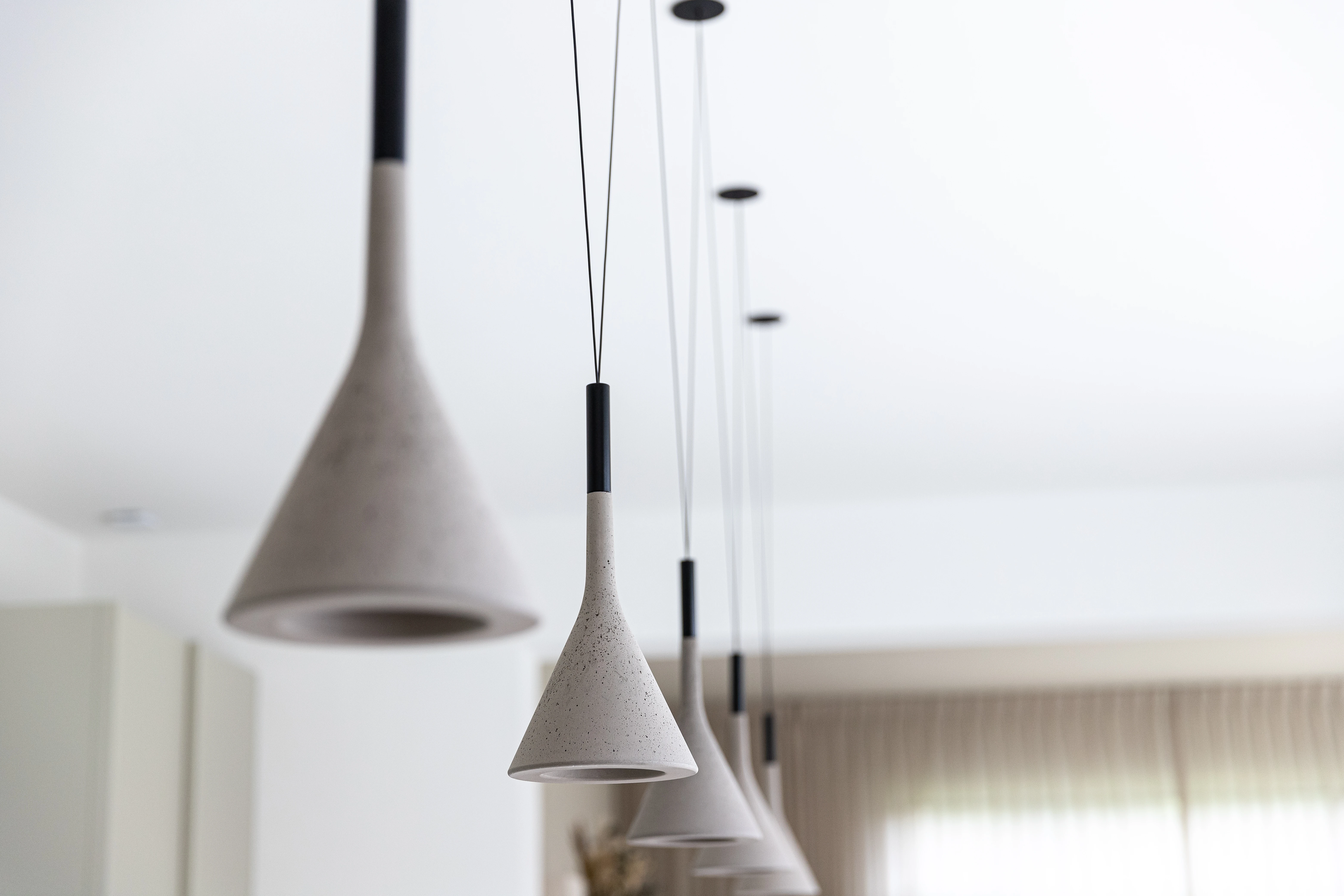 Detail van hanglampen van beton in een ruimte met lichte gordijnen