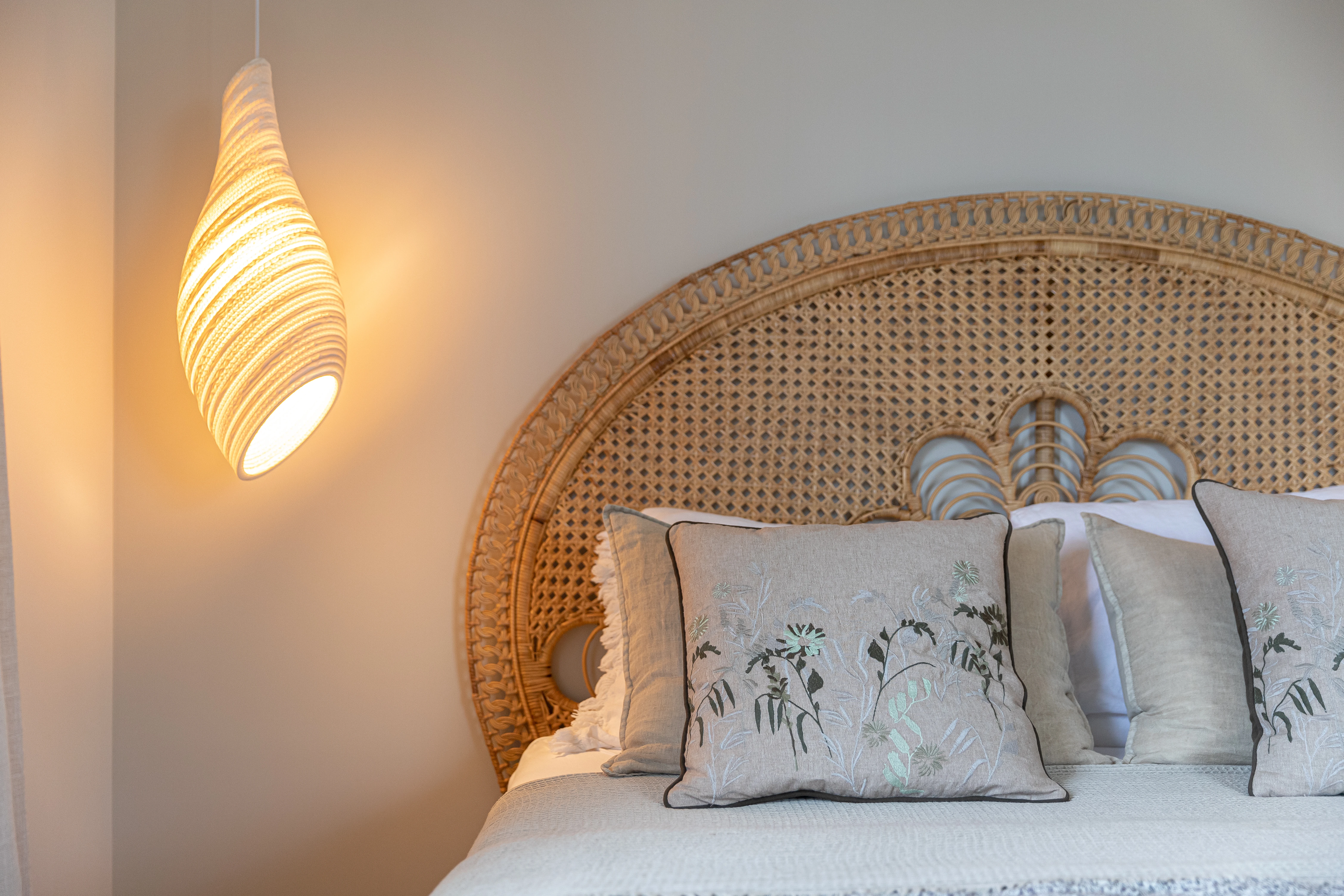 Slaapkamer met een hoofdeinde van rotan, geborduurde kussens en een warm verlichte hanglamp