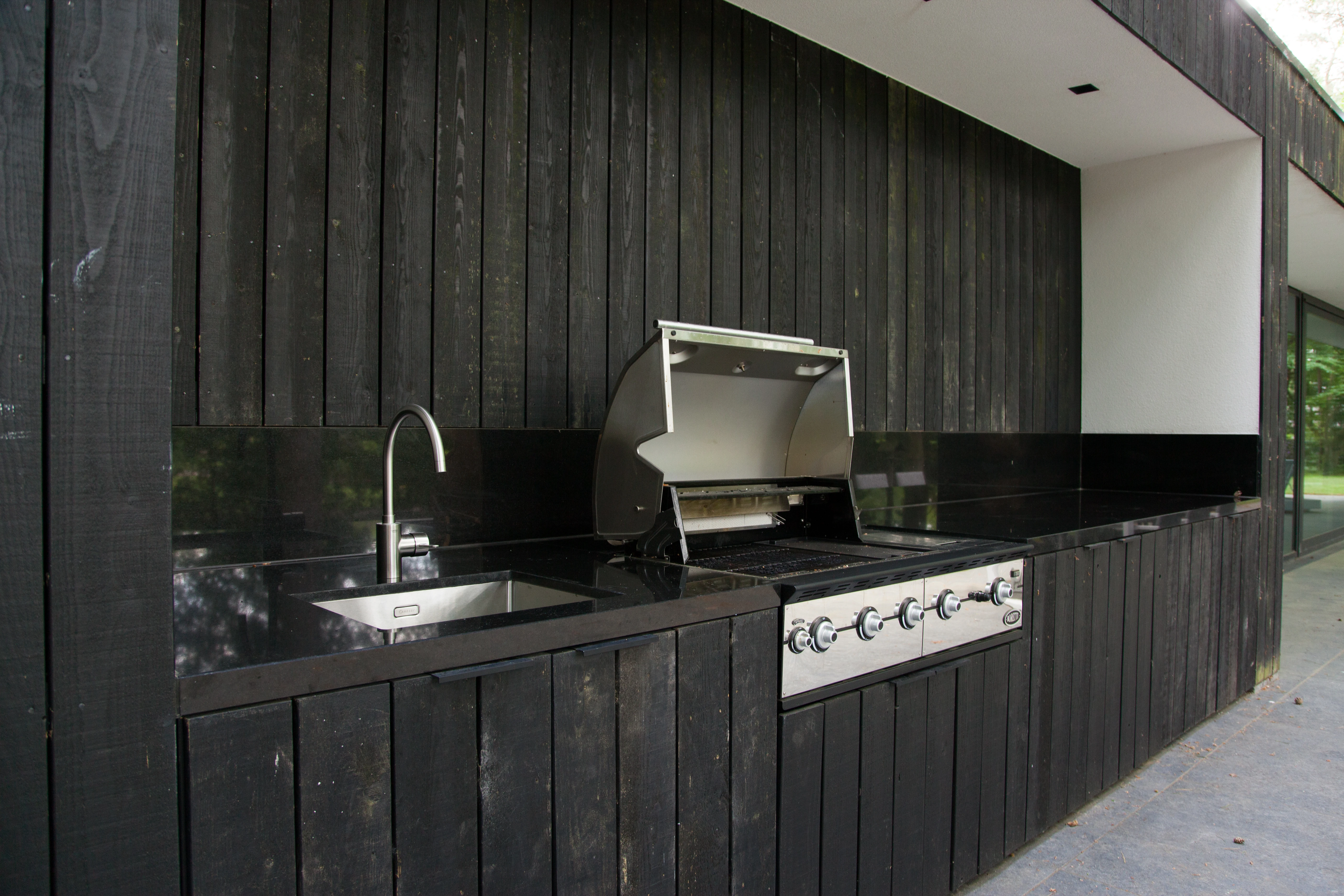 Buitenkeuken met zwart natuurstenen blad, spoelbak en ingebouwde barbecue
