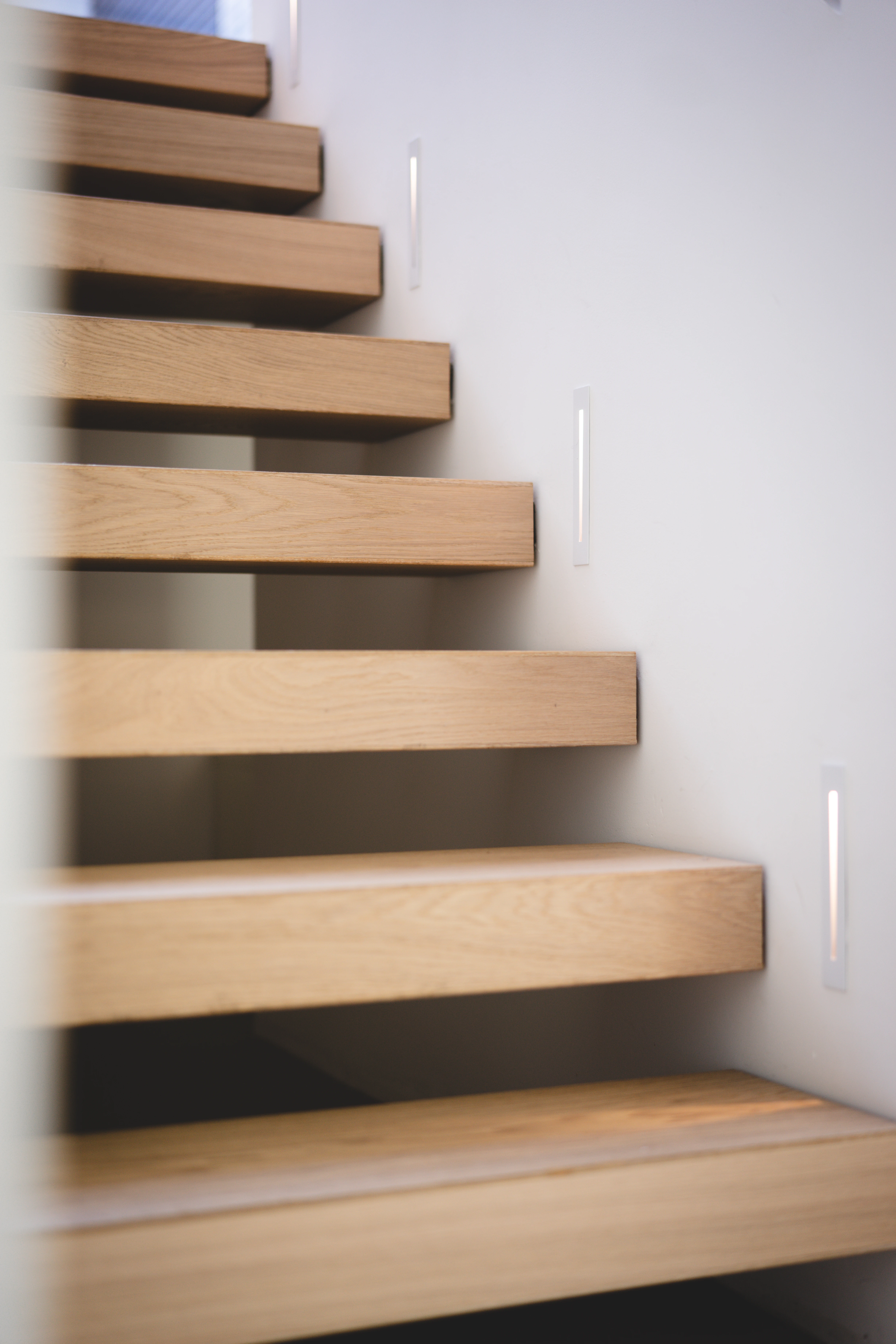 Detail van een zwevende eikenhouten trap met verlichting in de muur