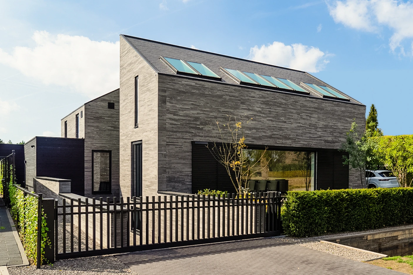 Voorgevel van een nieuwbouwvilla in Etten-Leur, grijs baksteenmetselwerk met dakramen en een zwart hekwerk