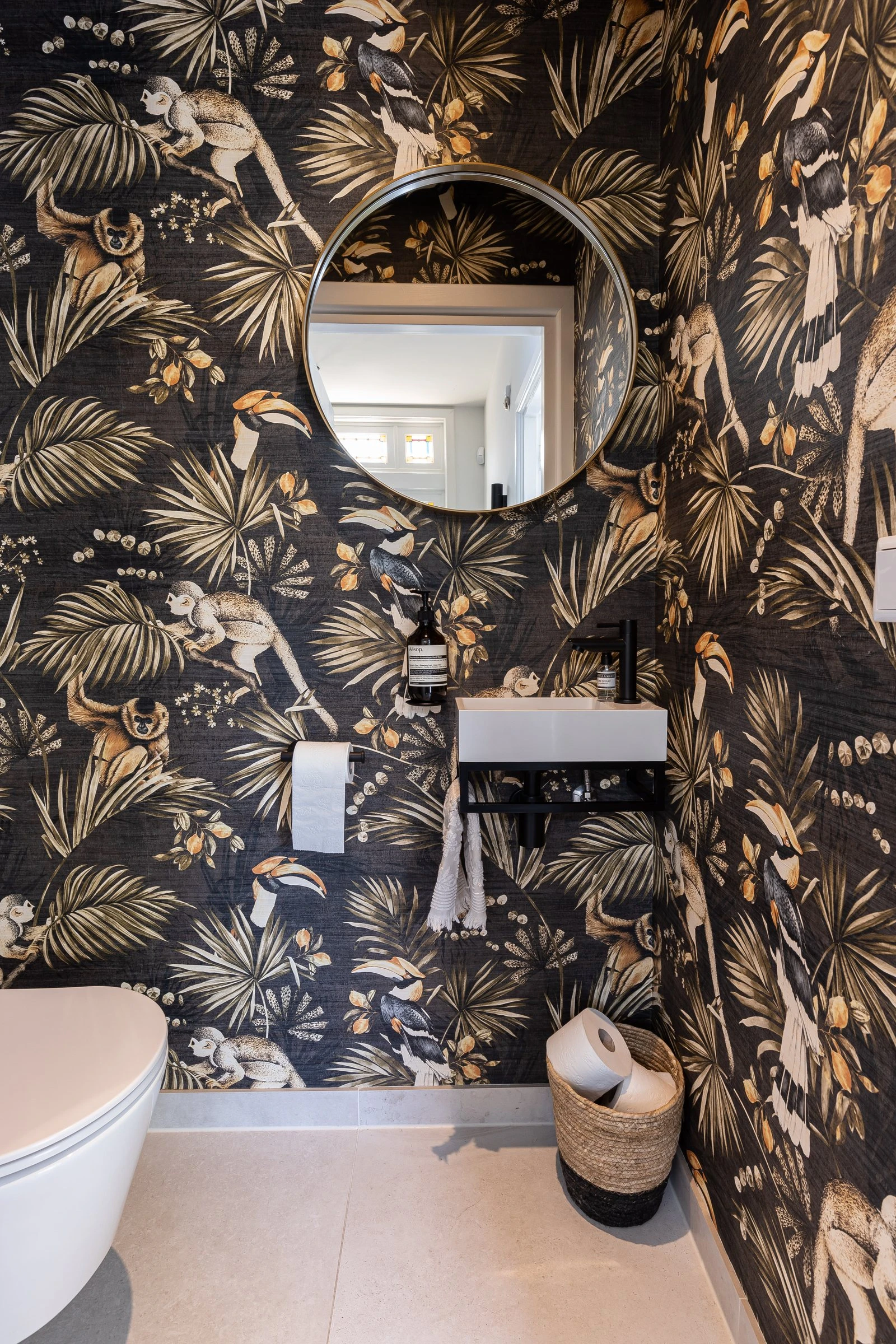 Toilet met jungle-behang en een ronde spiegel