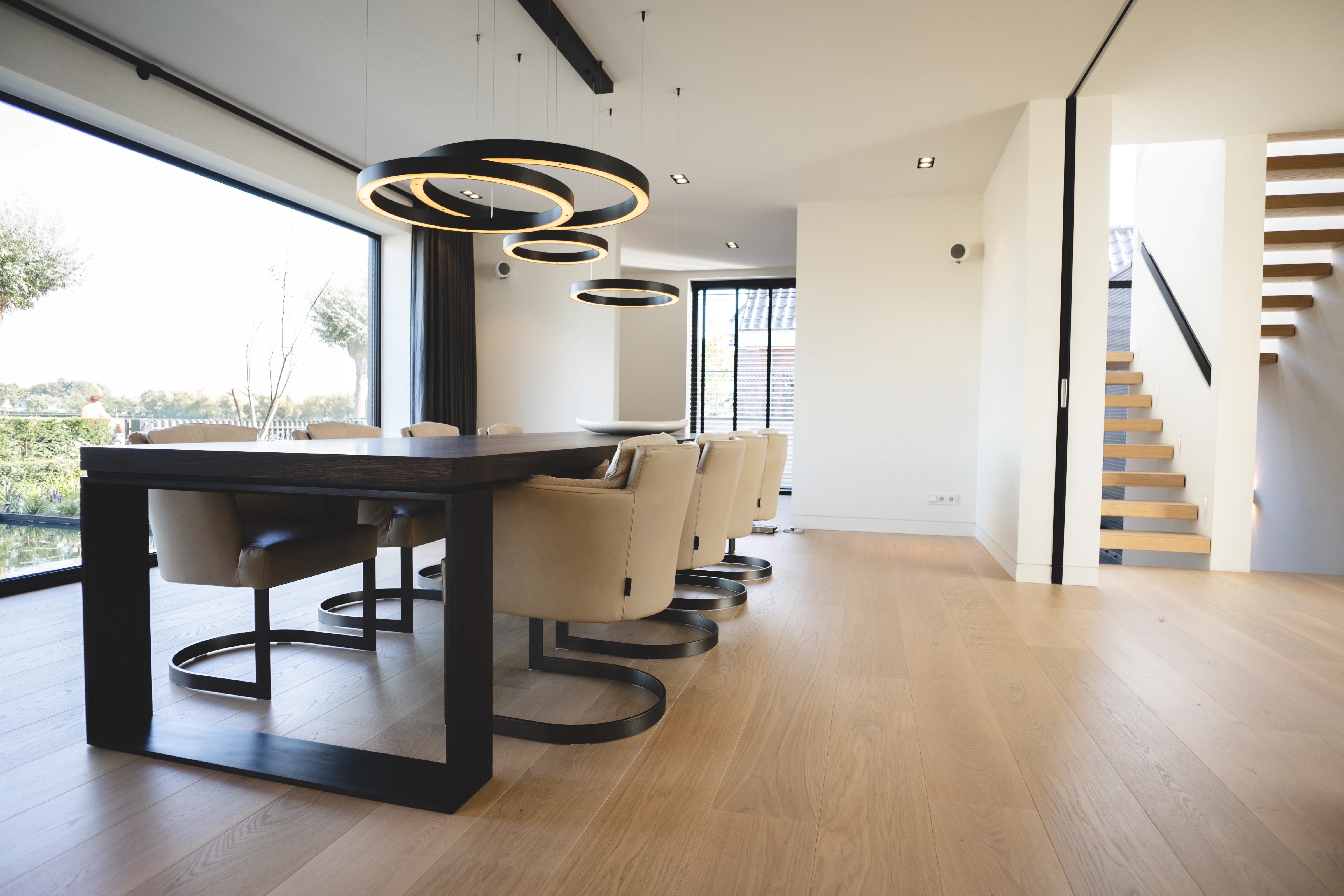 Eetkamer met donkere houten tafel en ronde hanglampen, met zicht op de trap
