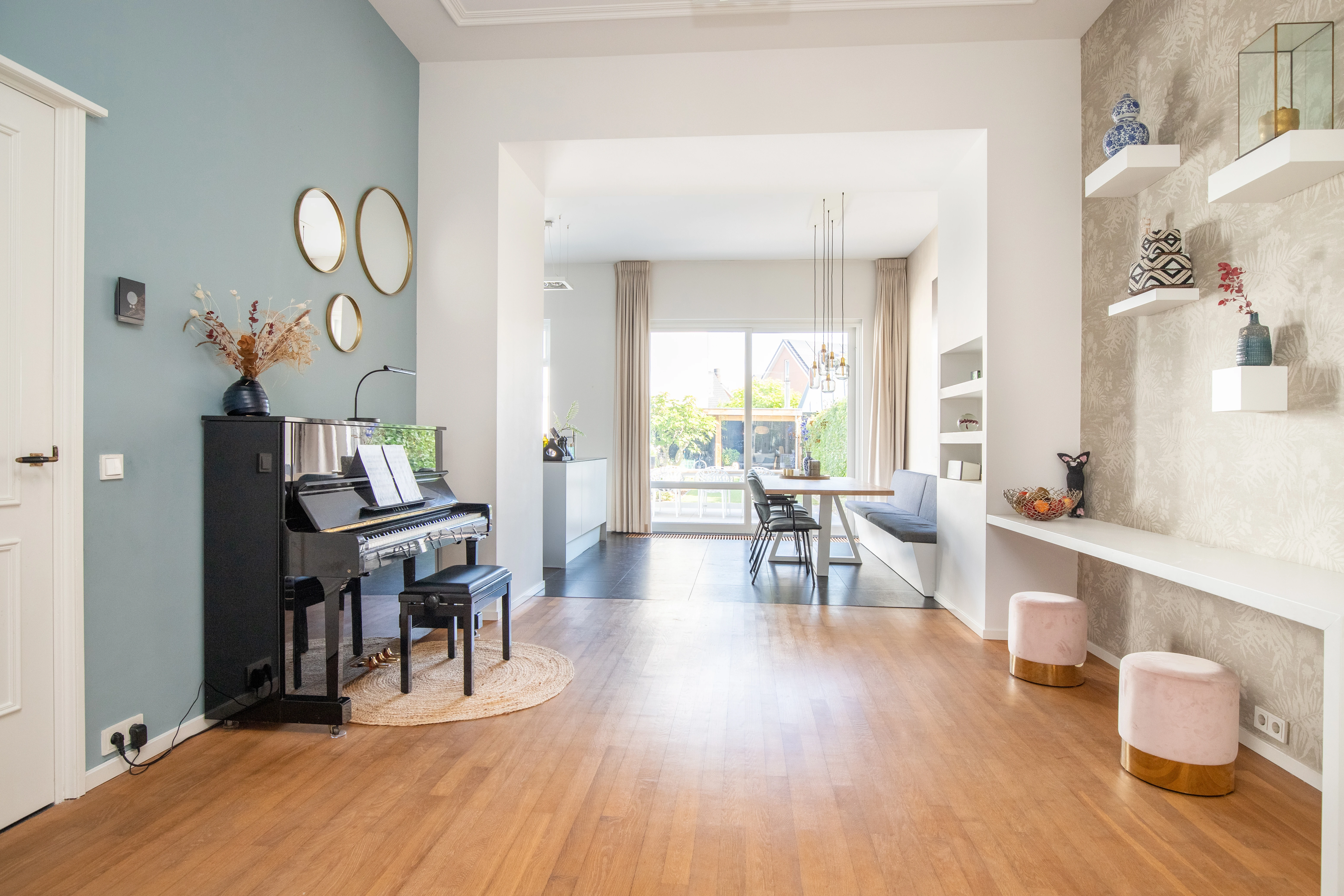 Zithoek met een piano tegen een lichtblauwe muur en een compositie ronde spiegels