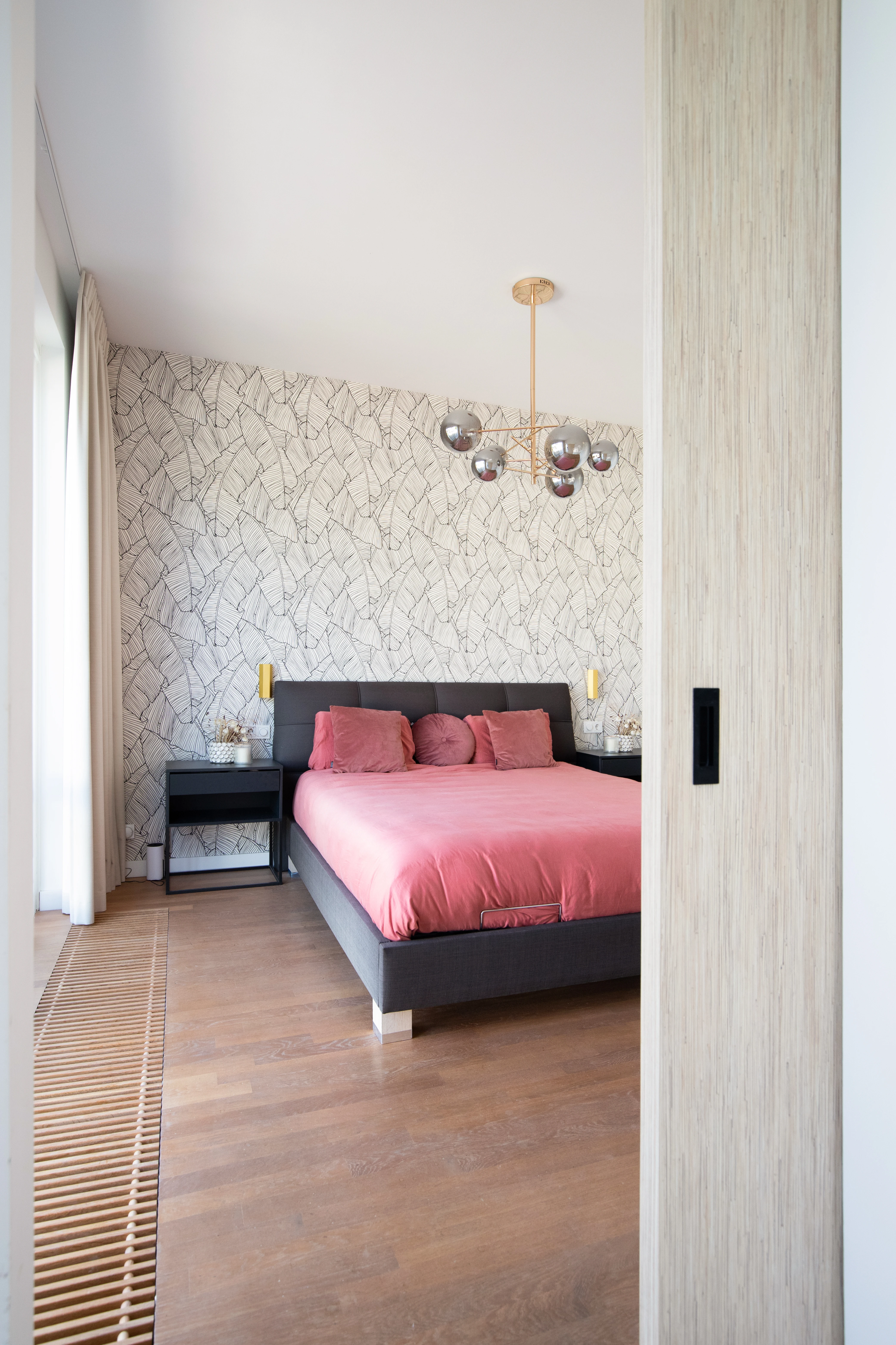 Slaapkamer met koraalkleurig beddengoed tegen een wand met bladmotief-behang
