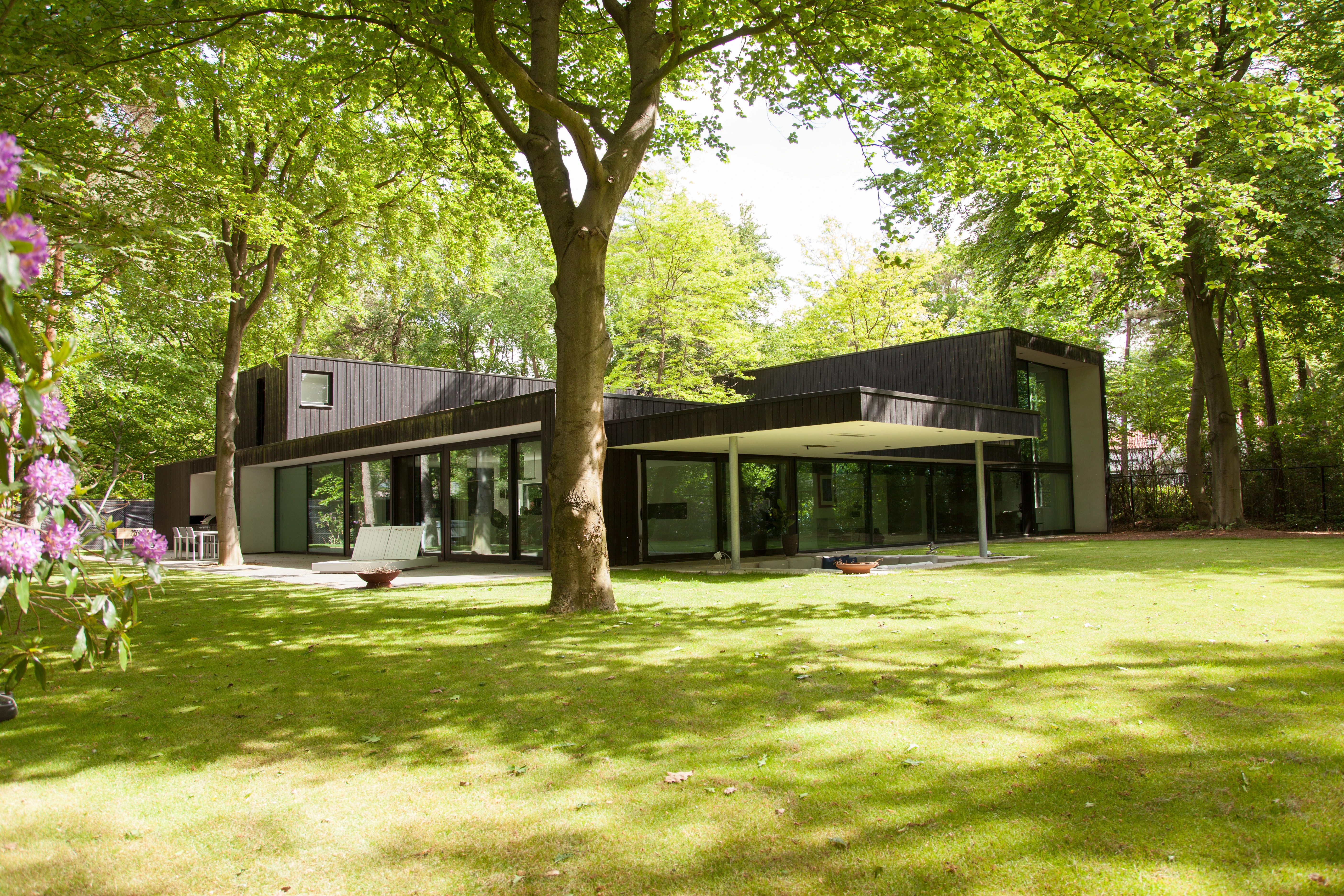 De villa met zwart gevelhout tussen de bomen, gezien vanaf het gazon