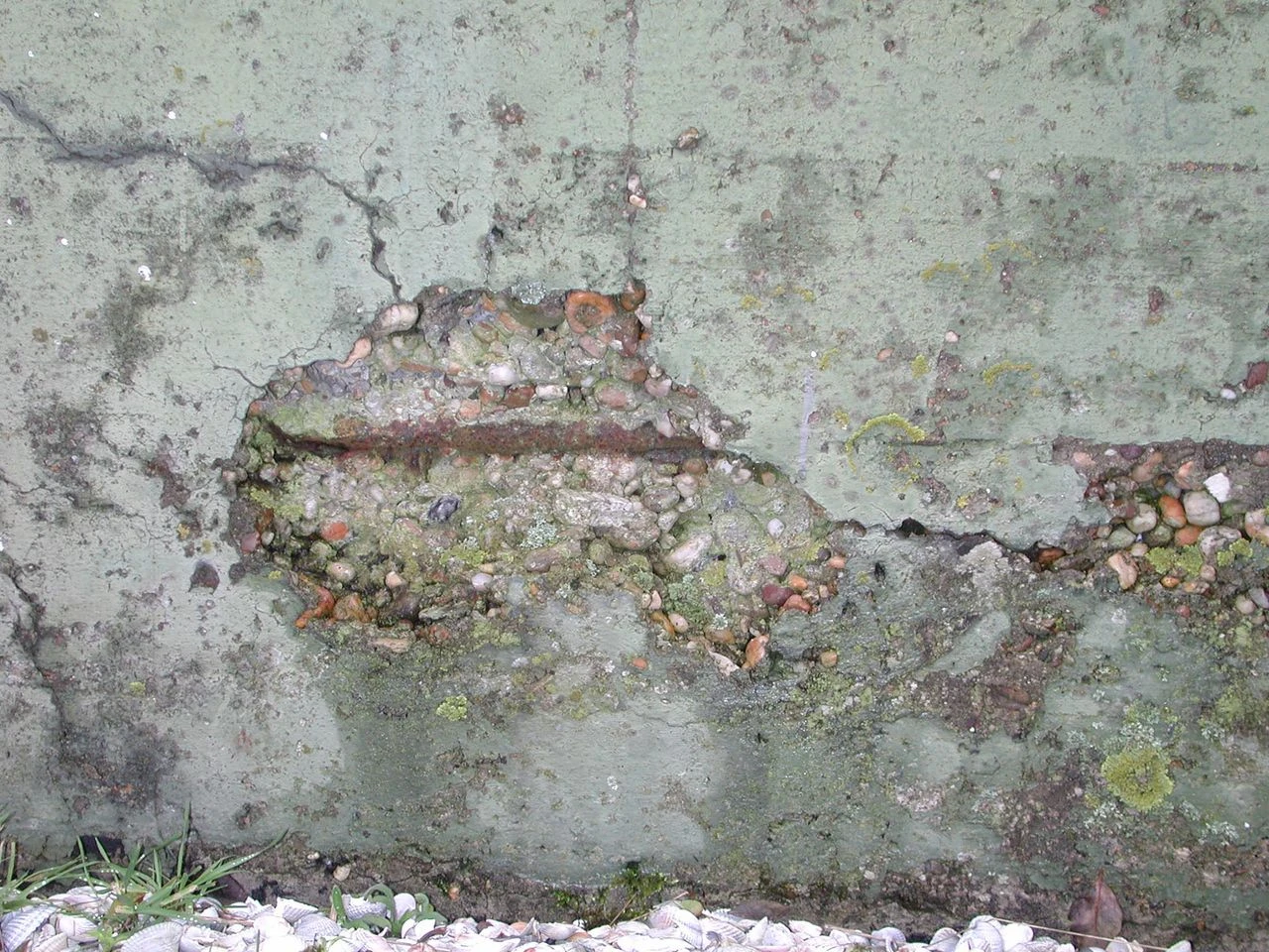 Betonschade aan een gevelmuur met afgebladderd beton en verroeste, blootliggende wapening