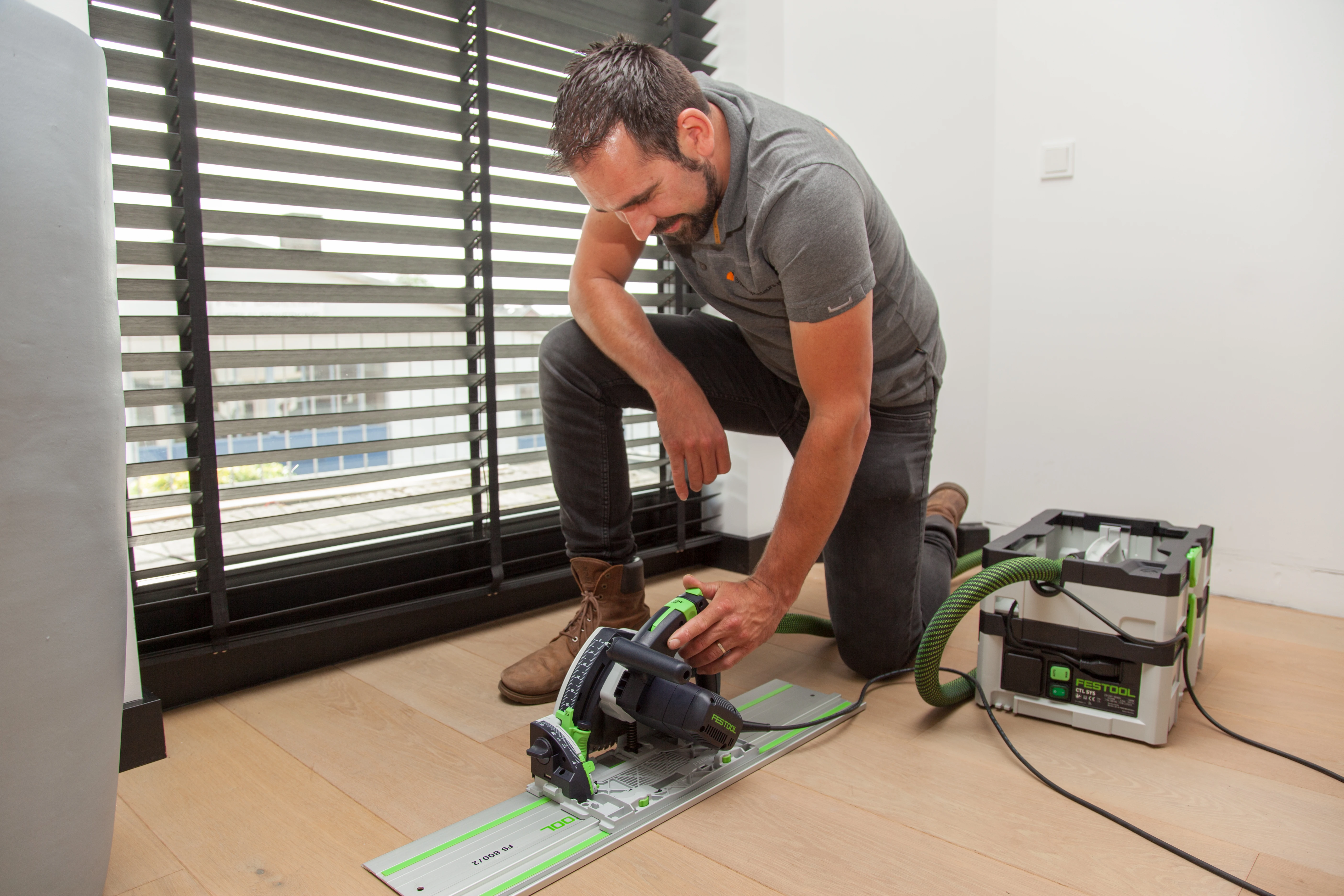 Inspecteur zaagt met een invalzaag met stofafzuiging een luik in een houten vloer